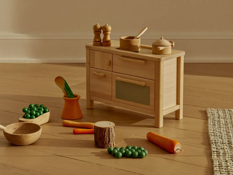 Illustration d'une petite cuisine en bois avec légumes miniatures posée sur le sol d'une salle de jeux